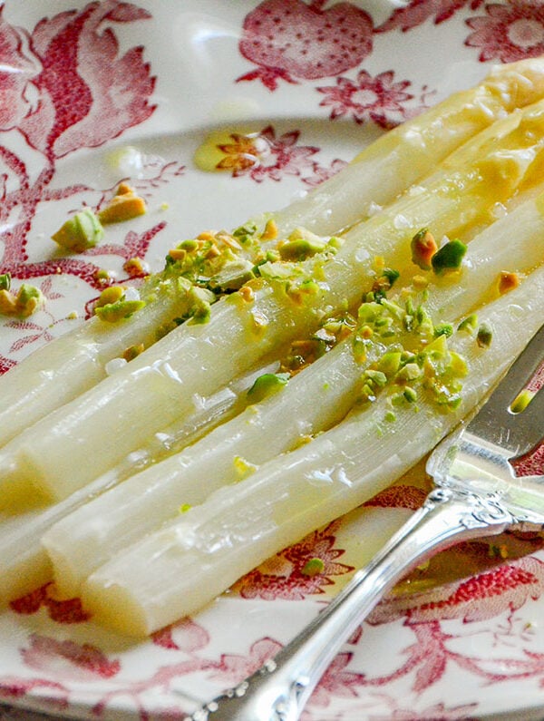 White asparagus on a pink plate with pistachios and a silver fork on the side