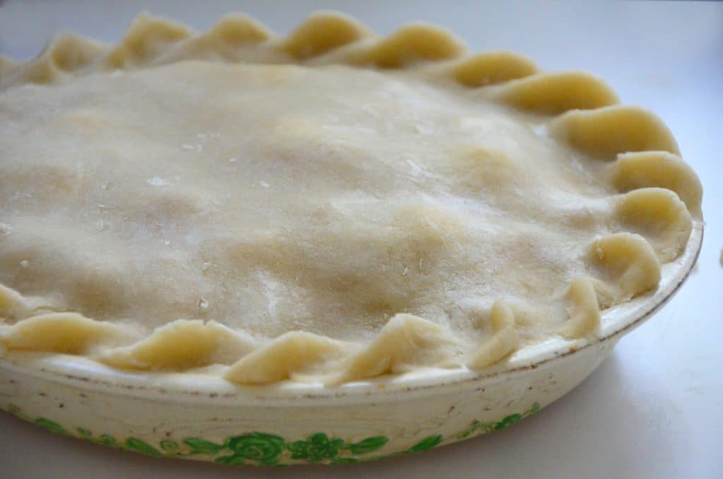 Raw pie crust top with fluted edge in a white pie plate with green trim