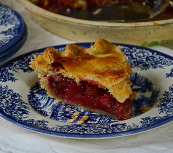 A slice of strawberry rhubarb pie with a golden crust on a blue plate