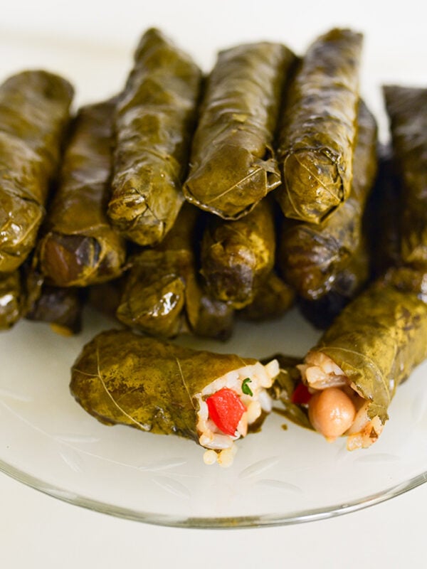 Vegetarian stuffed grape leaves with one cut open on a glass plate