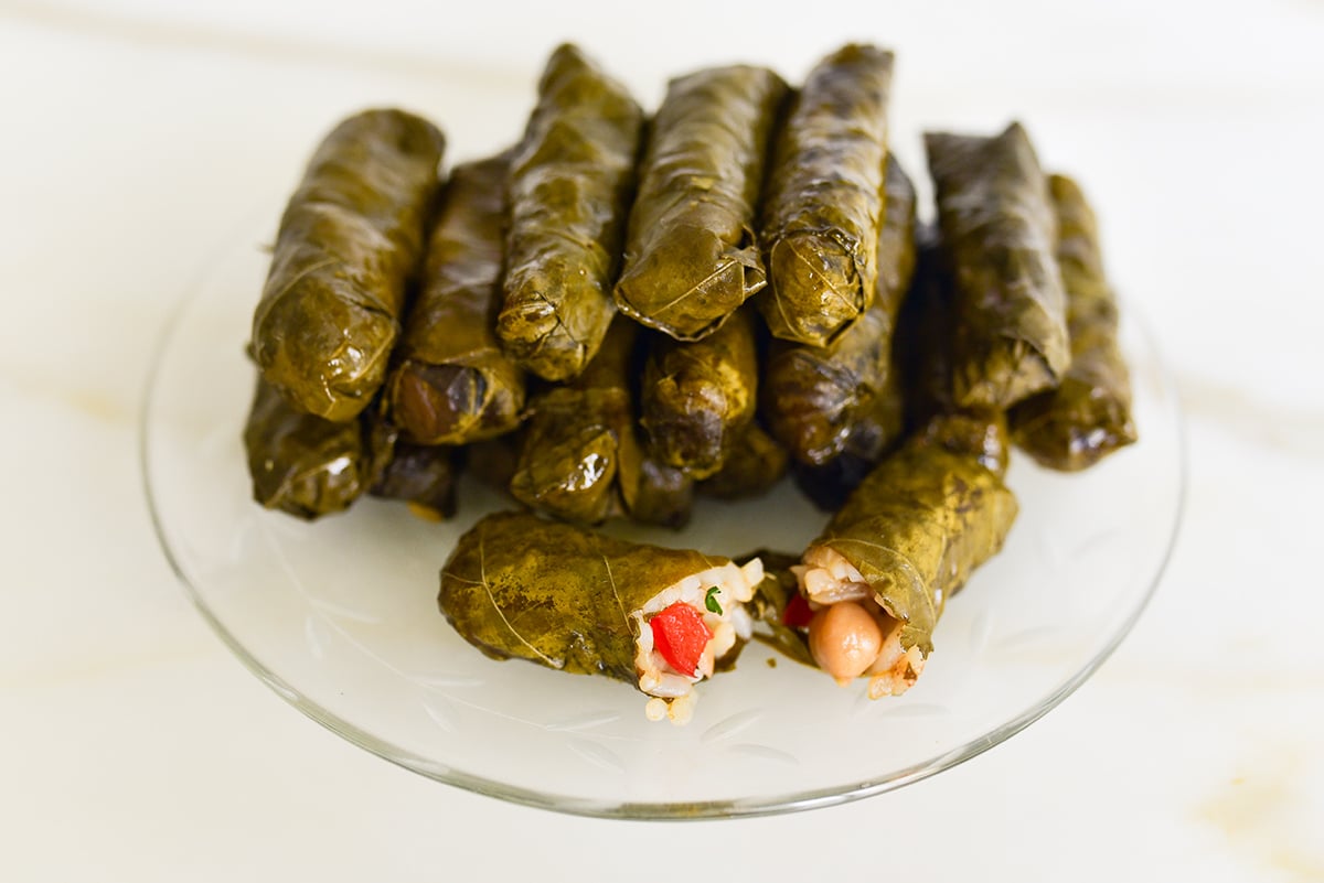Vegetarian stuffed grape leaves with one cut open on a glass plate