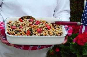 Square dish with barley picnic salad and a big spoon, in Mom's hands