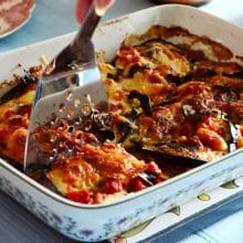 Eggplant parmesan with tomato sauce in a rectangular baking dish with a serving spoon