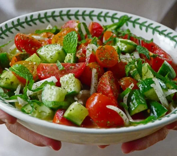 Cucumber Tomato Salad with mint in a round dish with hands holding it