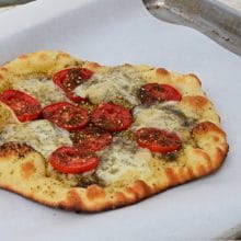 pizza with tomatoes and cheese on parchment on a sheetpan
