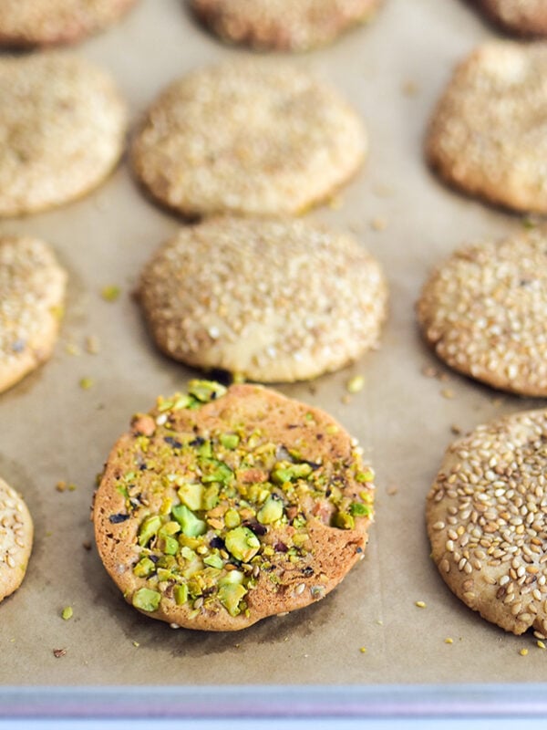 Sesame cookies on a parchment lined baking sheet with one turned over with pistachios on it