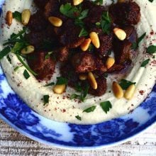 Hummus with lamb, sumac and pine nuts on a blue plate