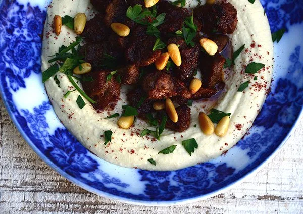 Hummus with lamb, sumac and pine nuts on a blue plate