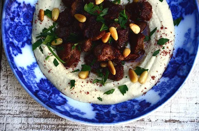 Hummus with lamb, sumac and pine nuts on a blue plate