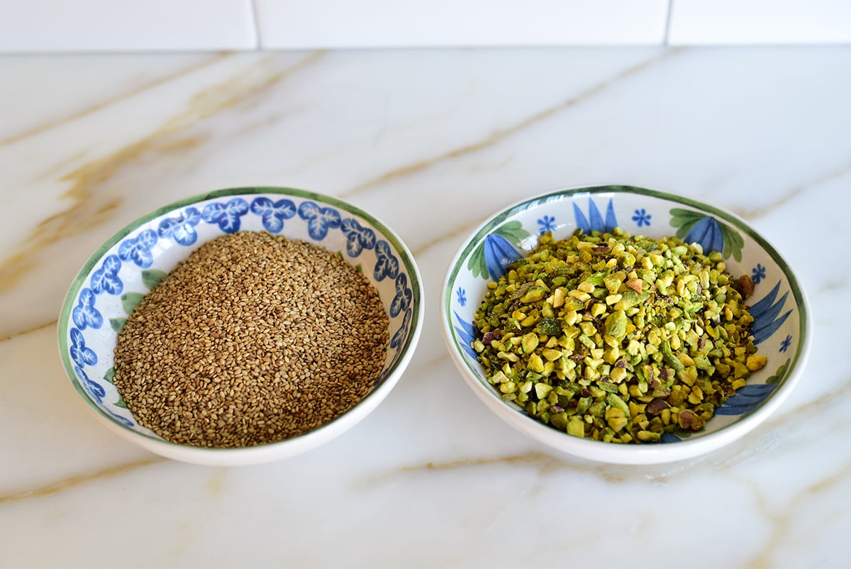 Two bowls side by side with sesame seeds in one and chopped pistachios in the other