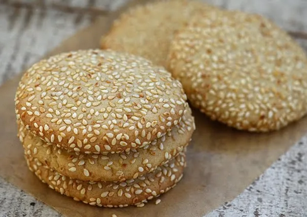 Cookies coated with sesame seeds in a stack on parchment paper