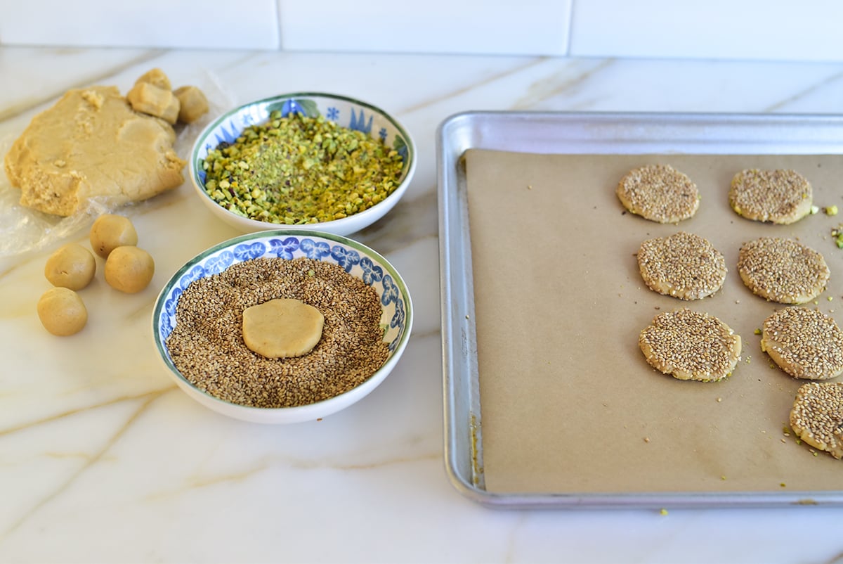 A disc of cookie dough in a bowl of sesame seeds with a baking sheet next to it