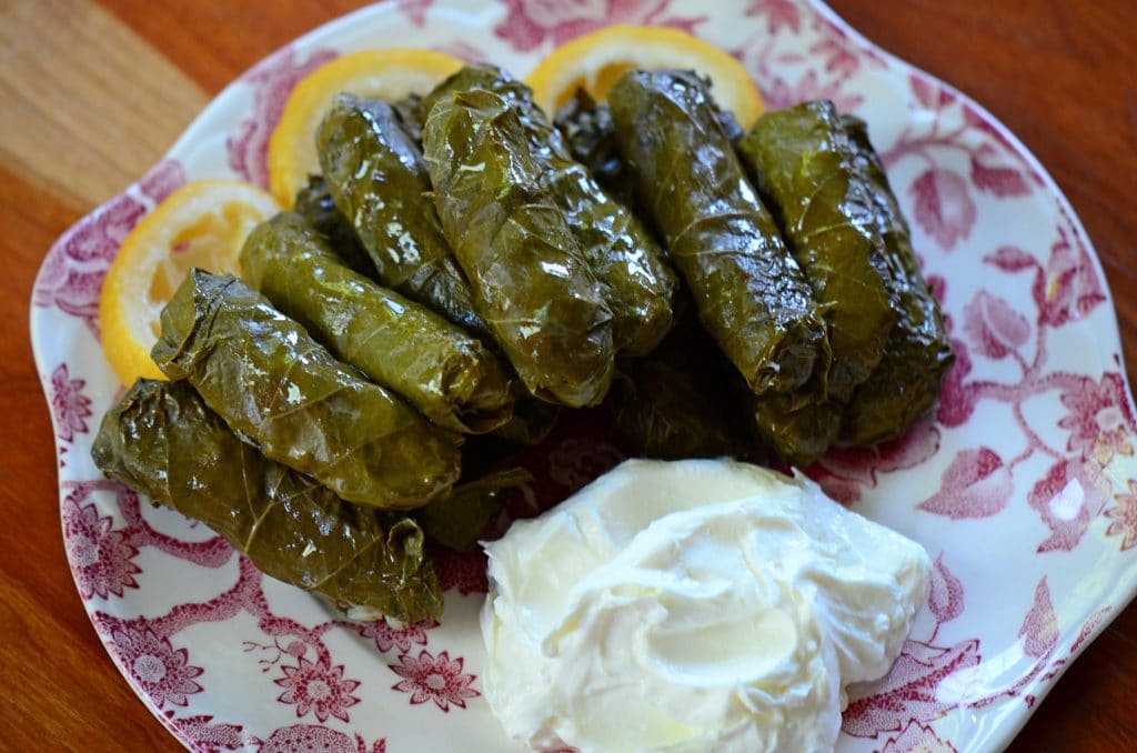 Stuffed grape leaves on a pink and white plate with labneh and lemon slices