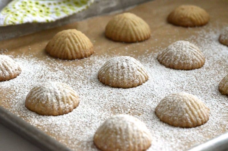 Baked Lebanese mamoul cookies being dusted with icing sugar.