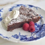 Dark chocolate torte with whipped cream and raspberries on a blue and white plate