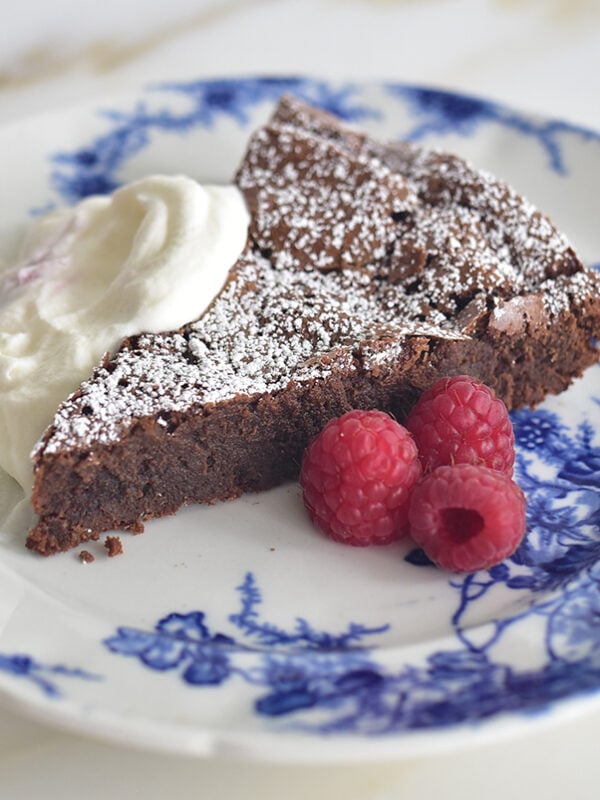 Dark chocolate torte with whipped cream and raspberries on a blue and white plate