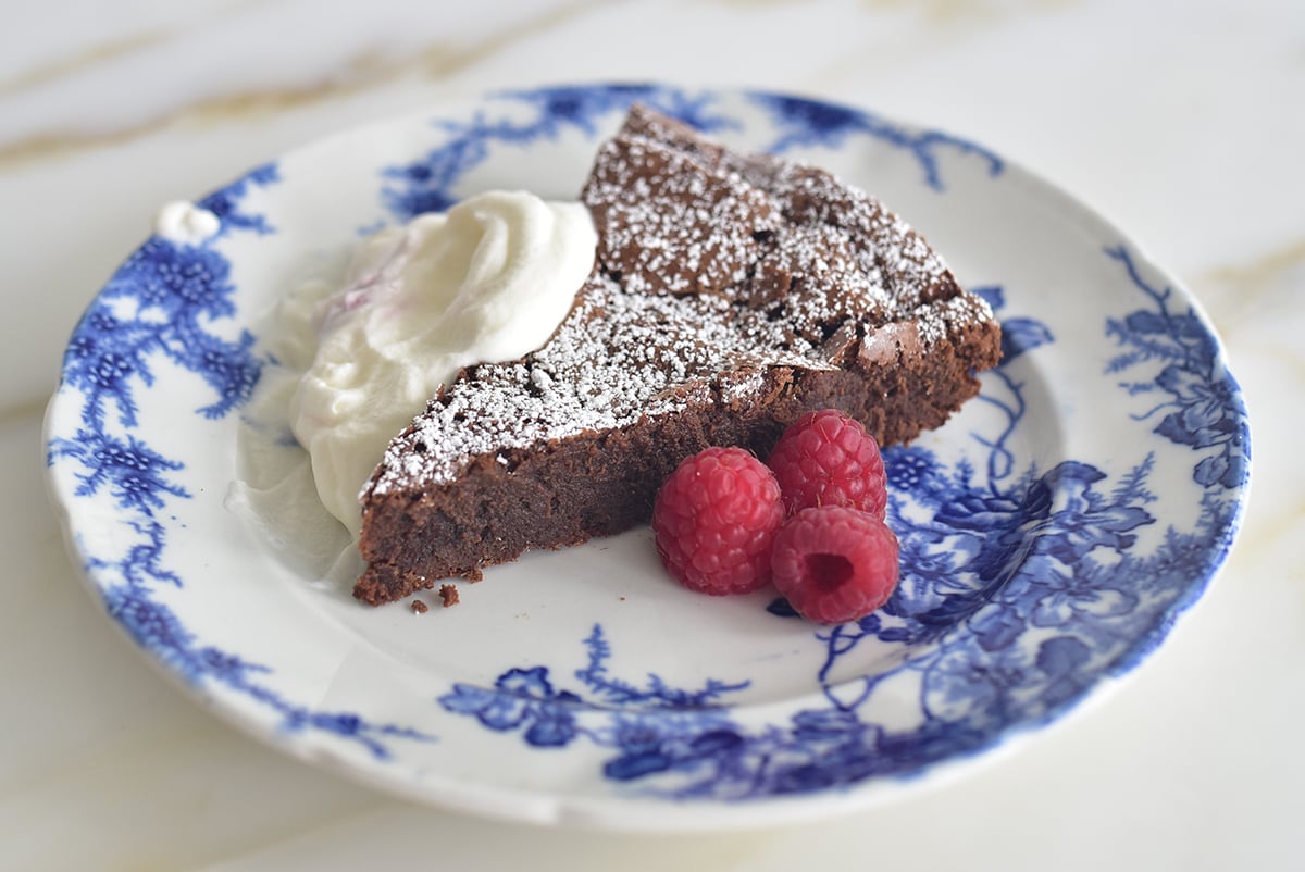 Dark chocolate torte with whipped cream and raspberries on a blue and white plate