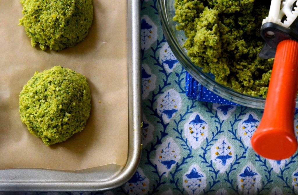 Homemade falafel is bright green with a mix of fresh herbs, scooped onto a sheet pan and ready to fry.