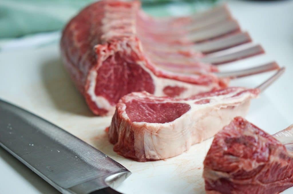 Rack of lamb sliced on a white cutting board with a knife