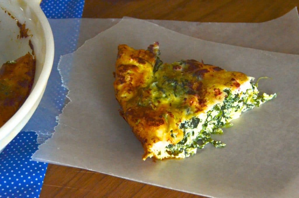 A slice of crustless quiche with spinach and feta on a piece of parchment paper.