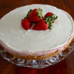 Strawberry cheesecake with white frosting and berries piled in the center on a wooden table