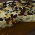 Olive bread on a wood board with slice next to it