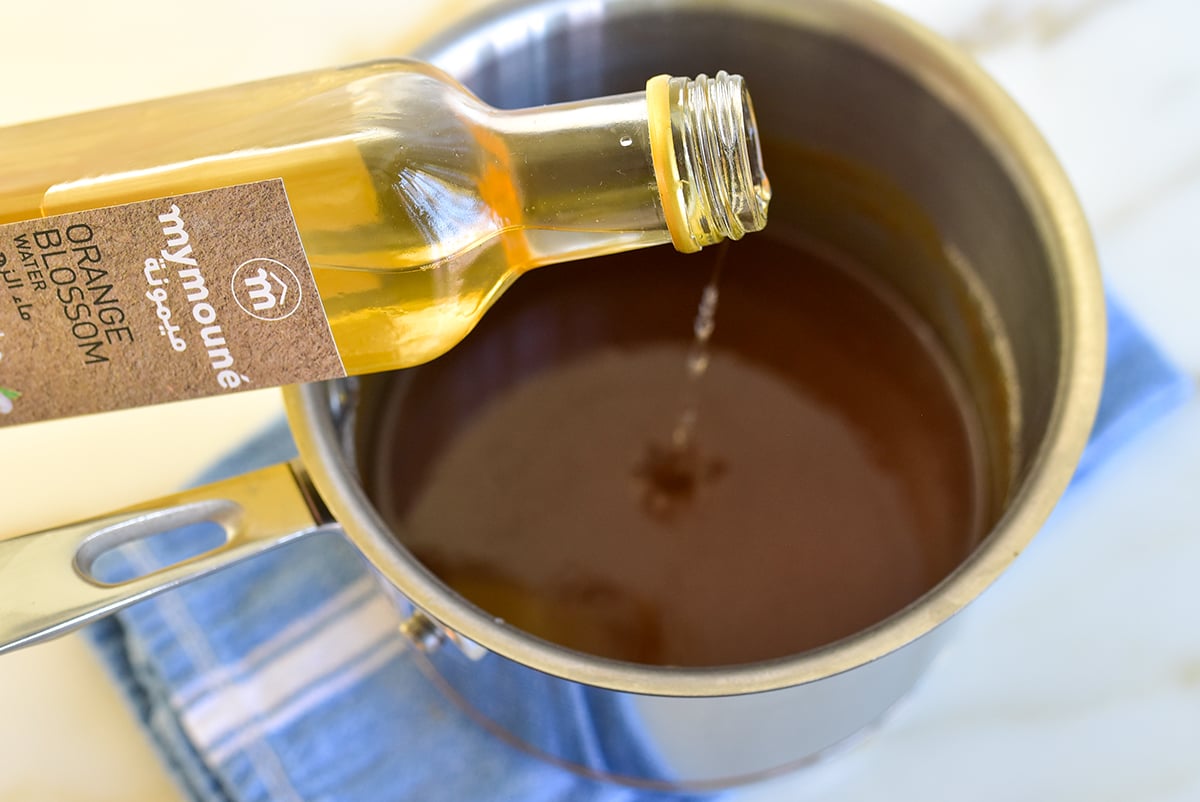 A bottle of orange blossom water poured into a pot of caramel sauce