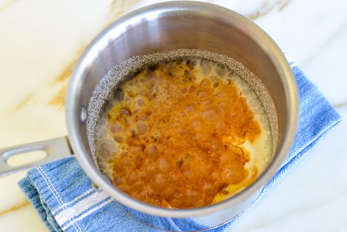 Bubbling caramel in a metal pot set on a blue towel