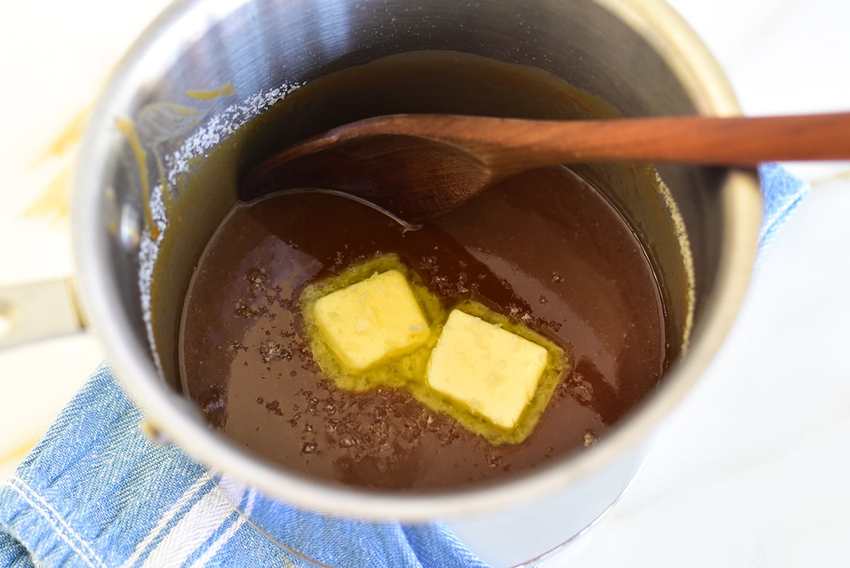 Homemade caramel in a pot with two pieces of butter and a wooden spoon in it