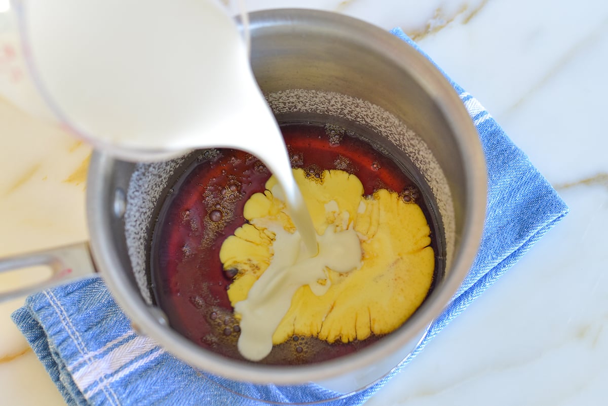 Cream pouring into a pot of caramelized sugar set on on a blue towel