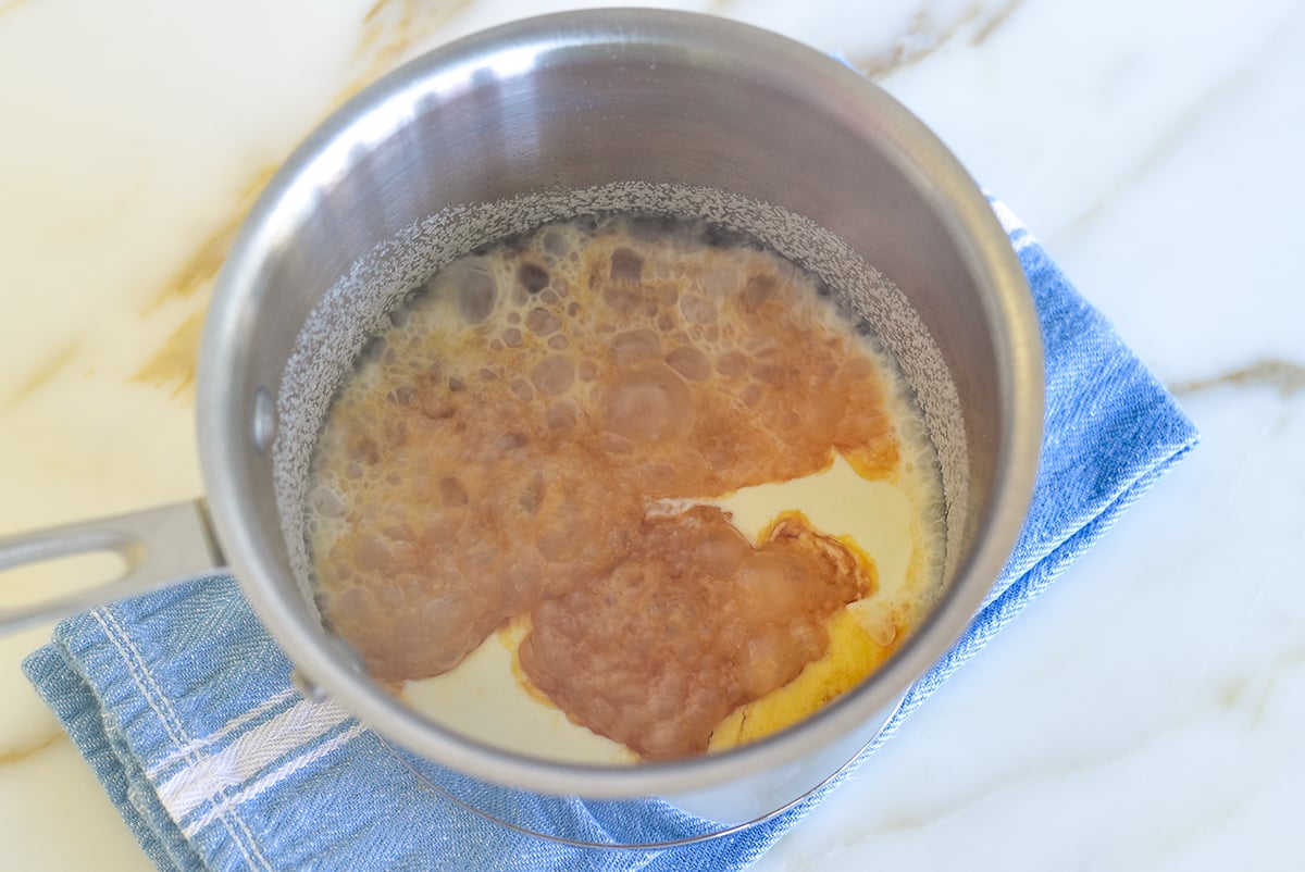 Steam rising from bubbling caramel with cream in it in a metal pot