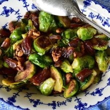 Brussels Sprouts with Dates and Walnuts in a blue dish with a silver spoon on the side