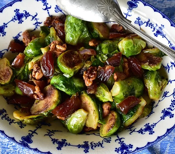Brussels Sprouts with Dates and Walnuts in a blue dish with a silver spoon on the side