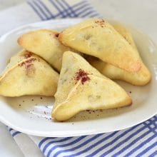 Triangle hand pies with a dusting of red sumac on top on a round white plate with blue striped napkin underneath