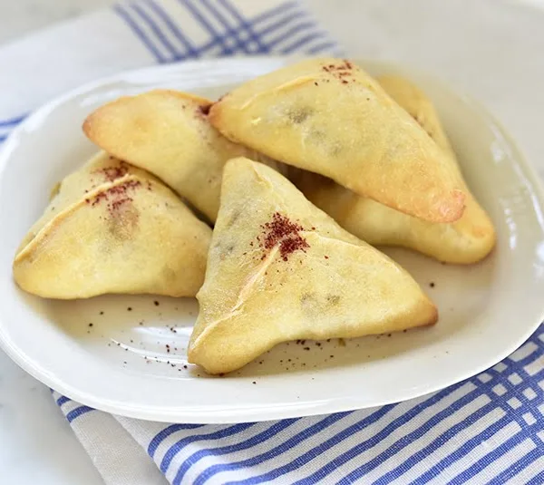 Triangle hand pies with a dusting of red sumac on top on a round white plate with blue striped napkin underneath