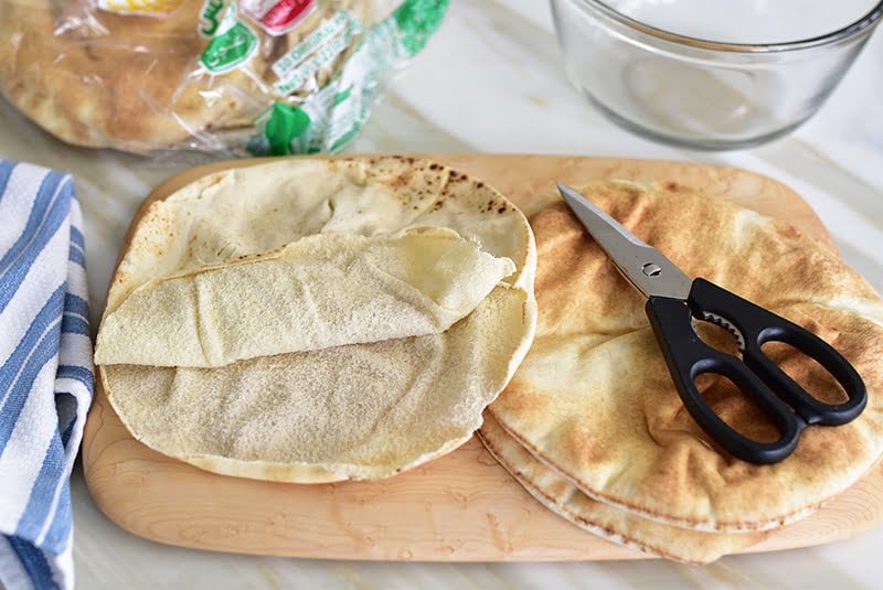 Pita breads on a wooden board with a pair of kitchen shears on top.