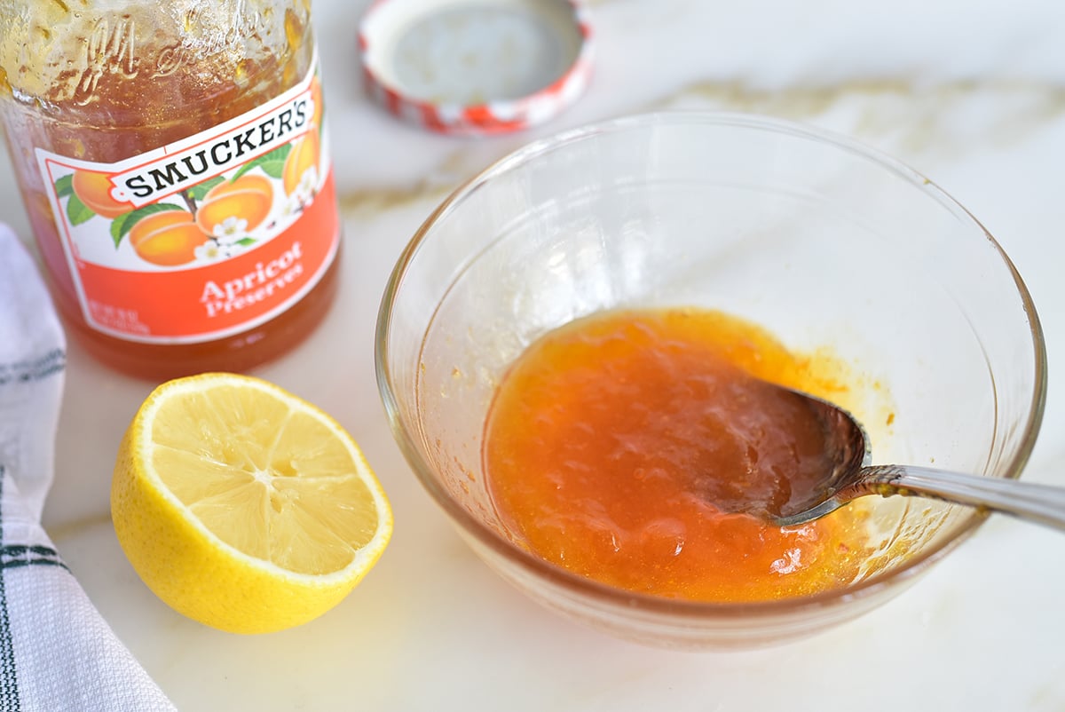 A glass bowl of apricot jam with a spoon in it and a lemon on the side