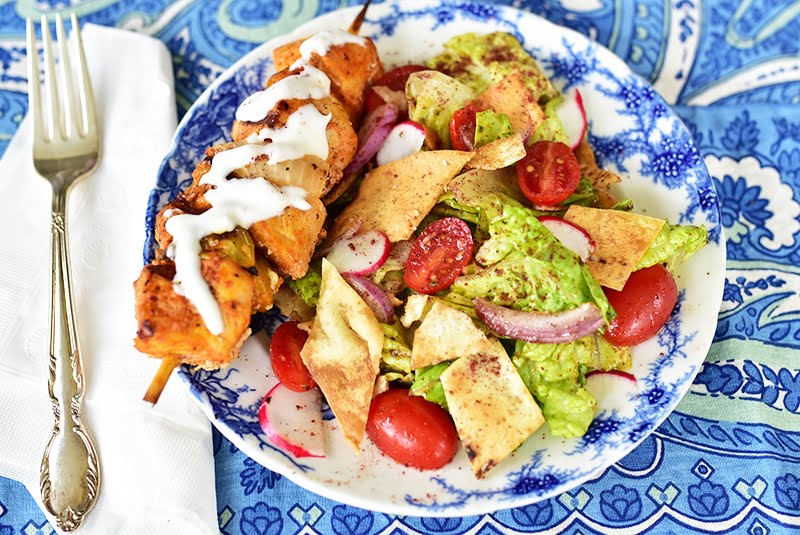 Fattoush salad with tomatoes and a chicken skewer with white sauce on a blue background plate