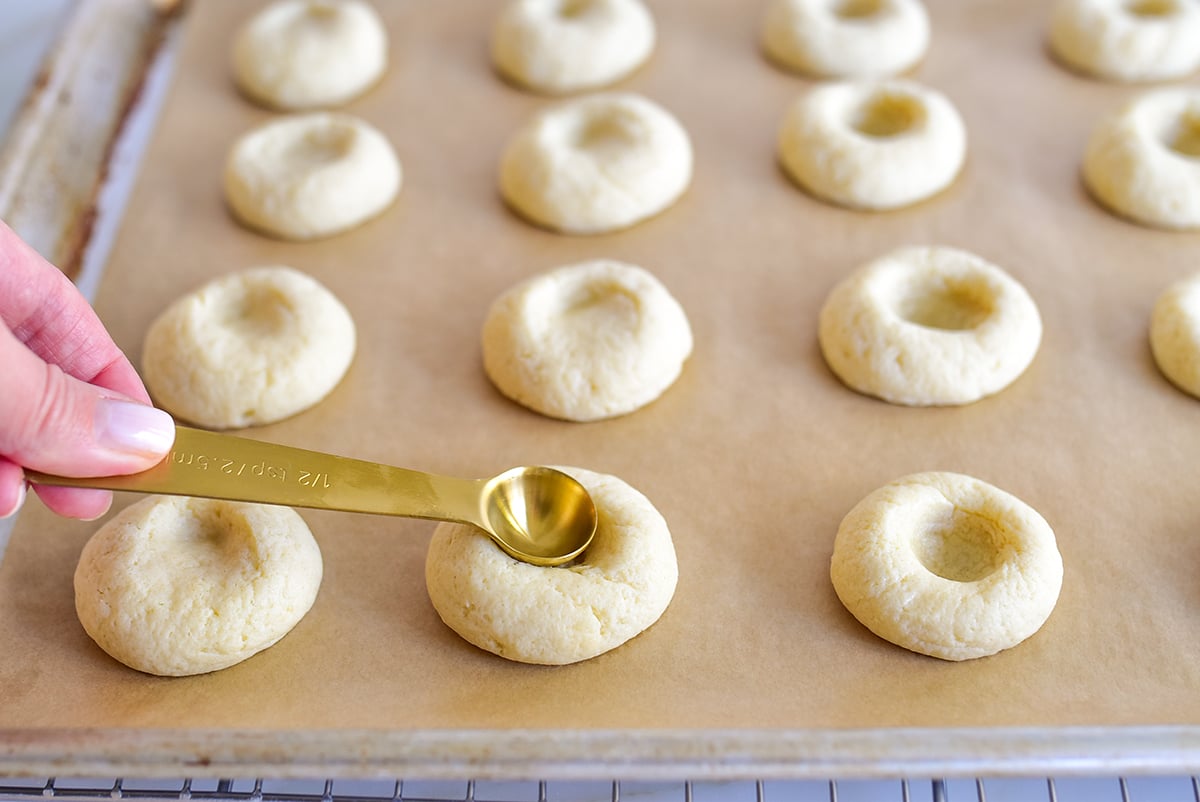 A teaspoon held by a hand making an indent in a dough ball for cookies