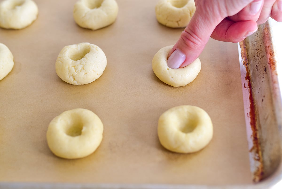 A thumb making an indent in a dough ball for thumbprint cookies
