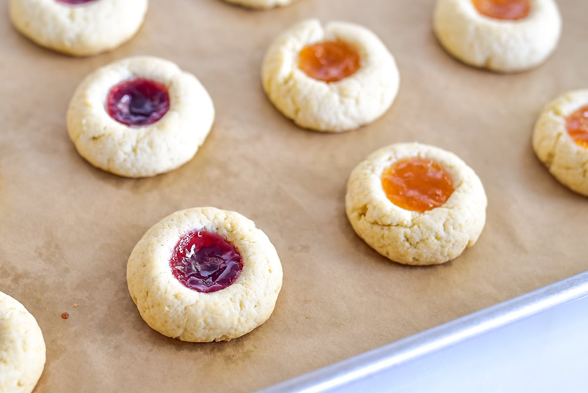 thumbprint cookies on parchment paper on a baking sheet with jam