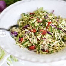 Cabbage slaw in a big white salad bowl with silver serving spoons