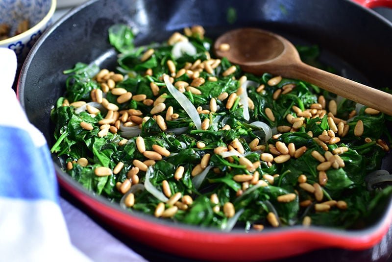 Satueed spinach with pine nuts in a cast iron skillet with a wooden spoon.