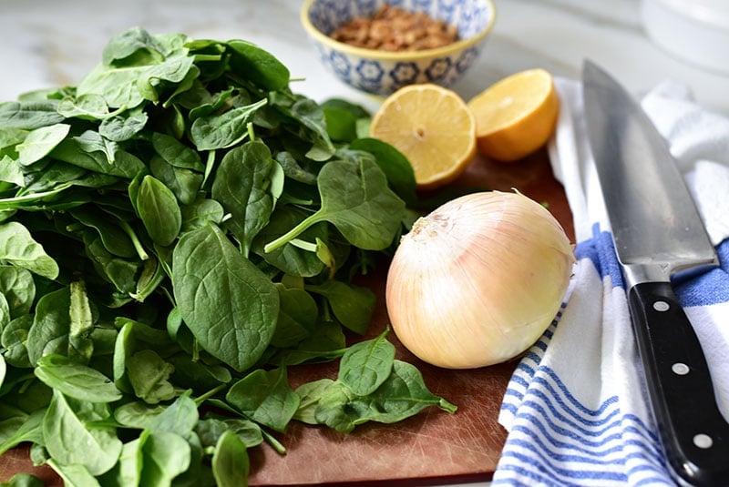 Spinach, an onion, and lemon halves on a wooden cutting board.