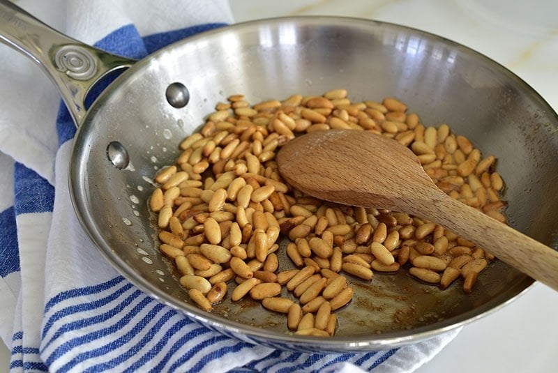 Pine nuts being toasted in a stainless steel pan.