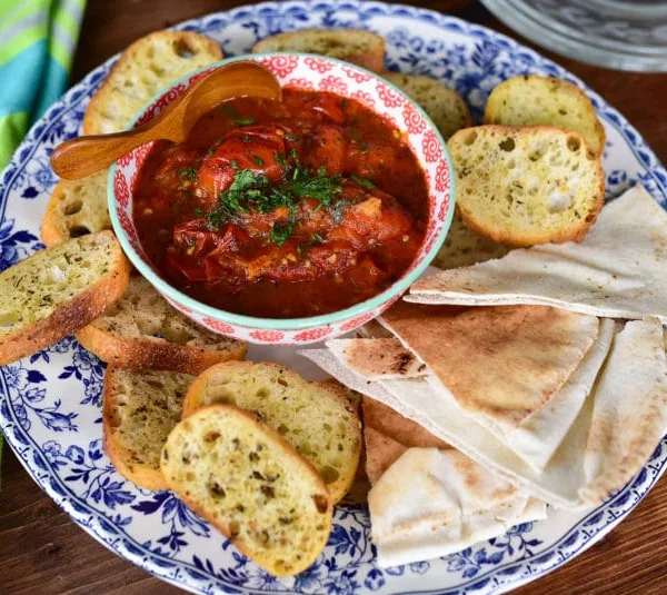 Tomato salsa topped with fresh mint in a bowl, surrounded by pita bread on a platter