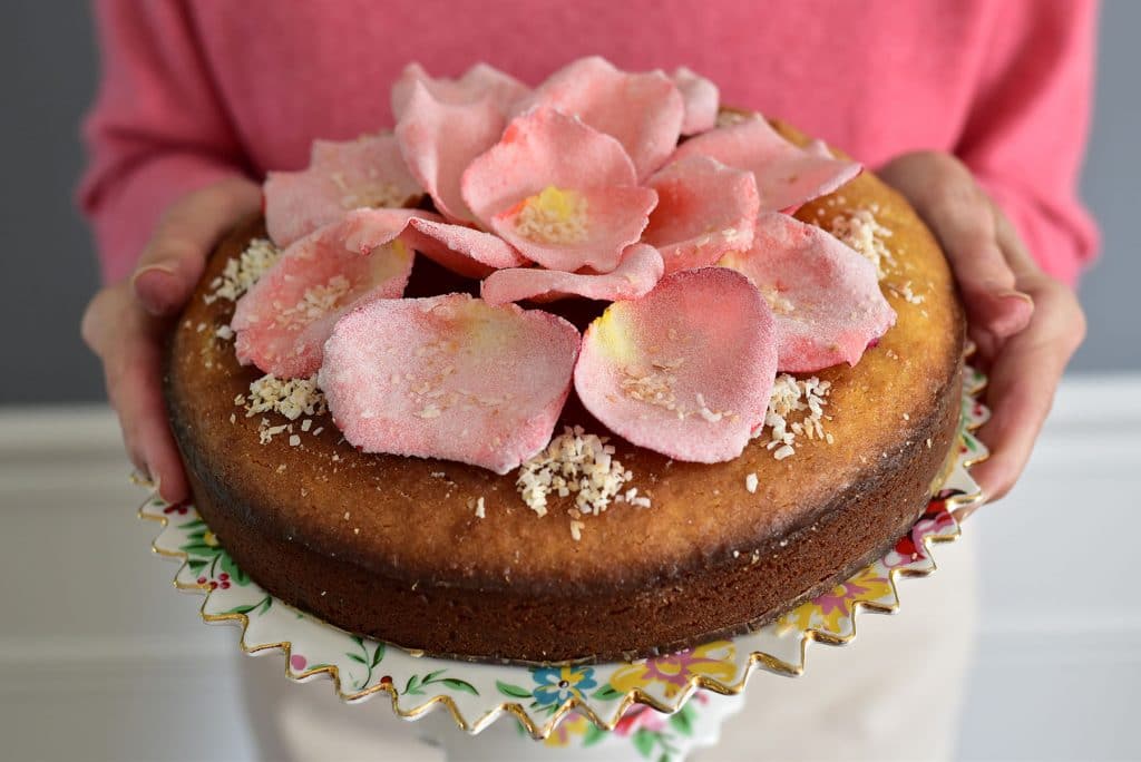 Mom holding a cake plate with cake and pink sugared rose petals arranged on top