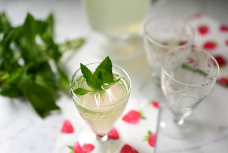 Fresh mint lemonade with fresh mint sprigs in small glasses on a strawberry printed napkin.