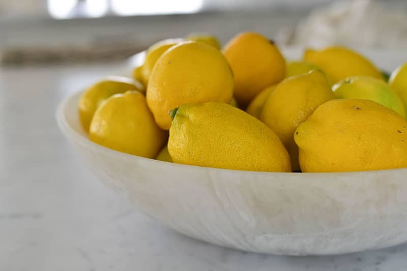 Many yellow lemons in a white bowl on the marble counter, Maureen Abood.com