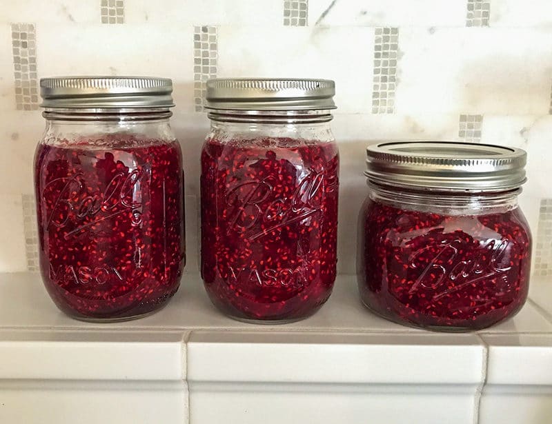 Raspberry jam in jars on a tile kitchen shelf.